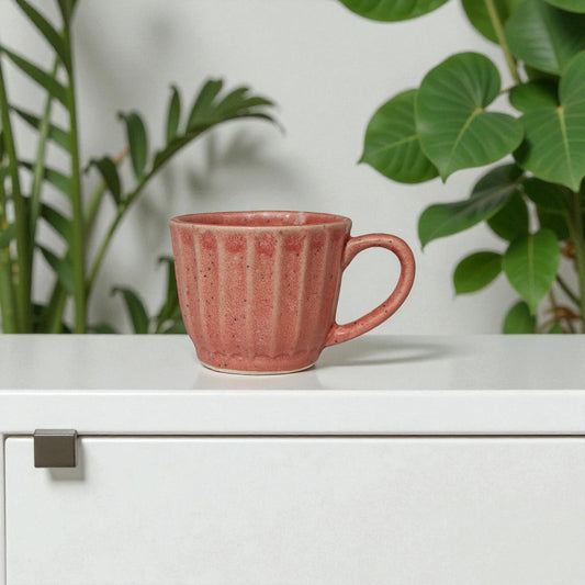 Pink mug on a white surface with green plants in the background