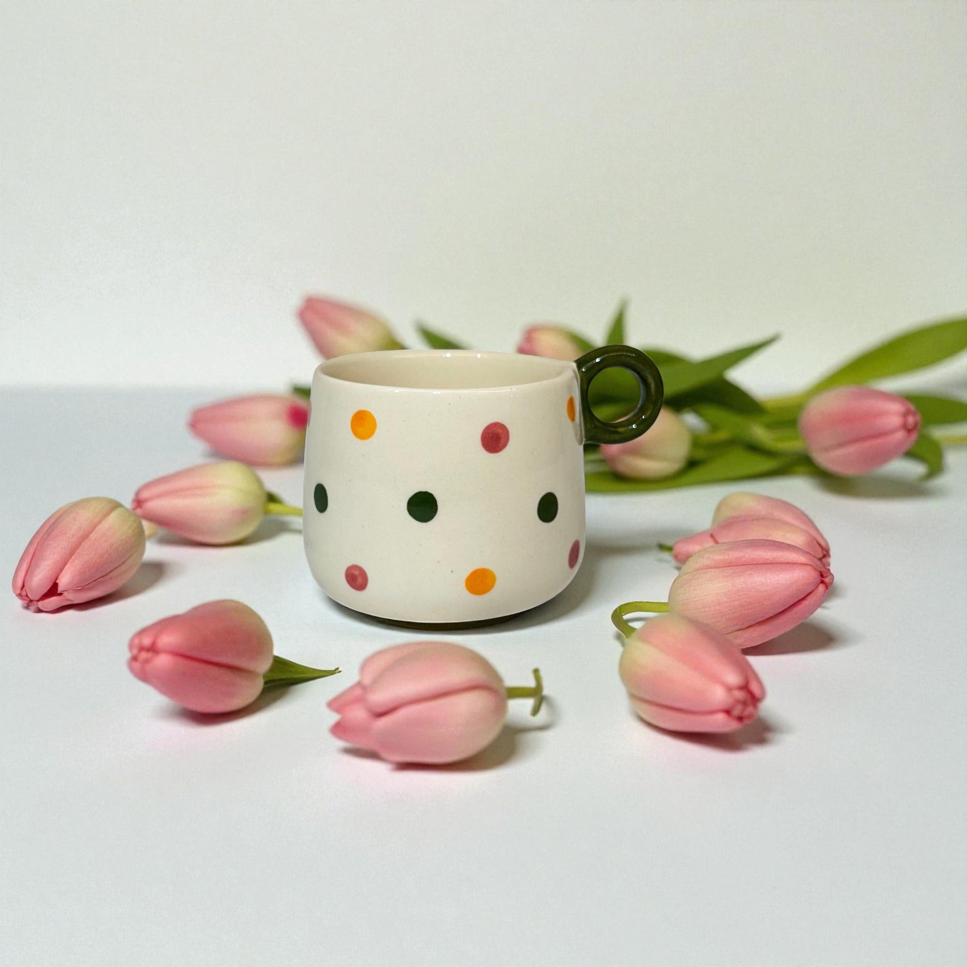 Polka dot mug with a black handle surrounded by pink tulips on a light background