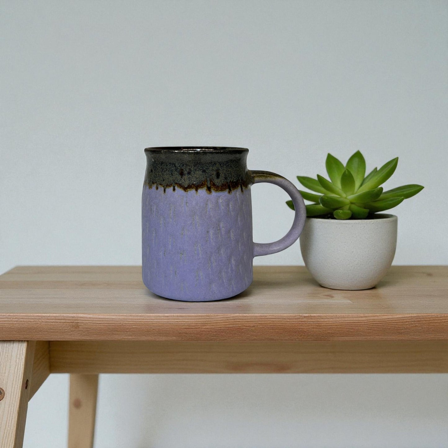 Purple mug with black rim on a wooden table next to a small potted plant.