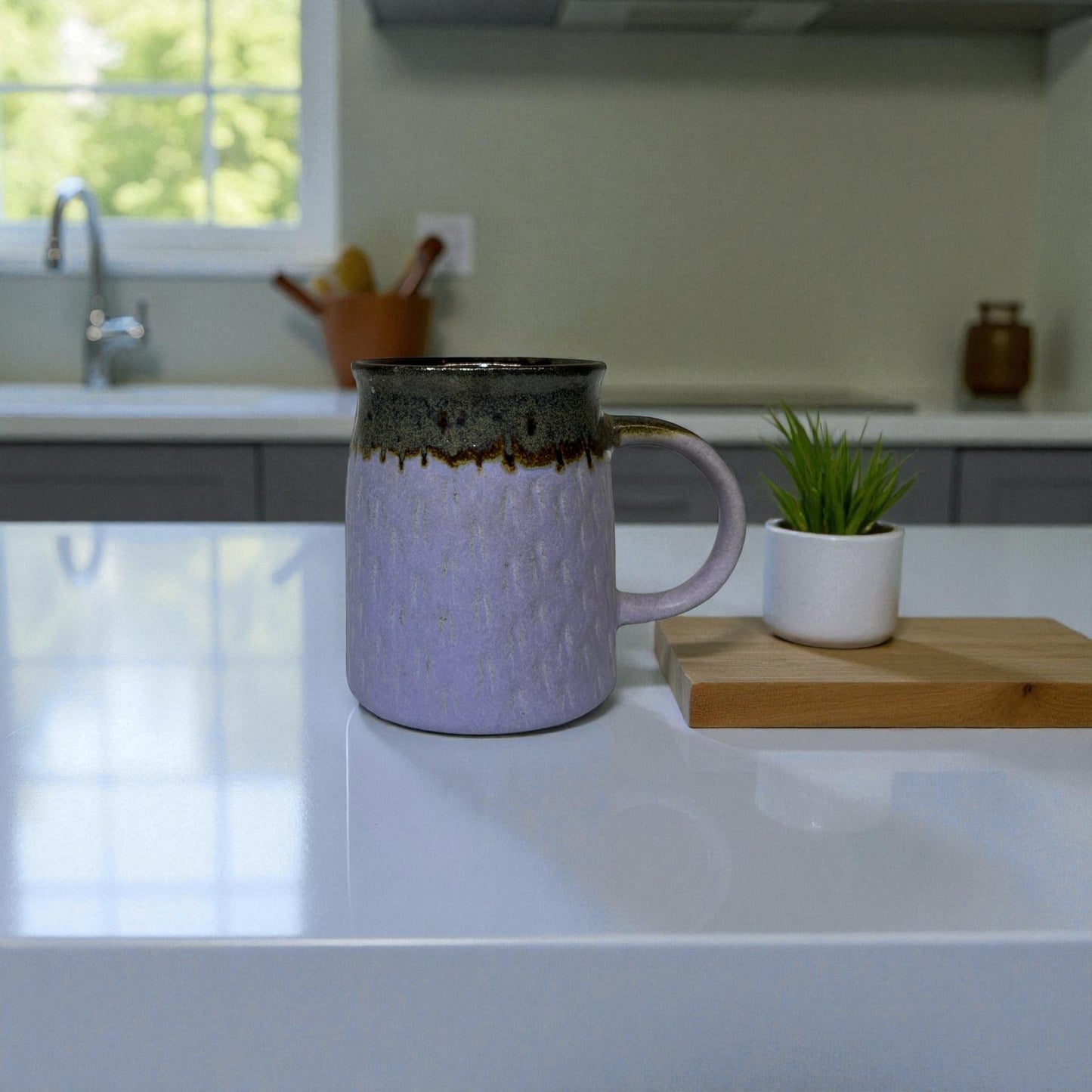 Purple mug with brown accents on a kitchen counter with a plant and cutting board.