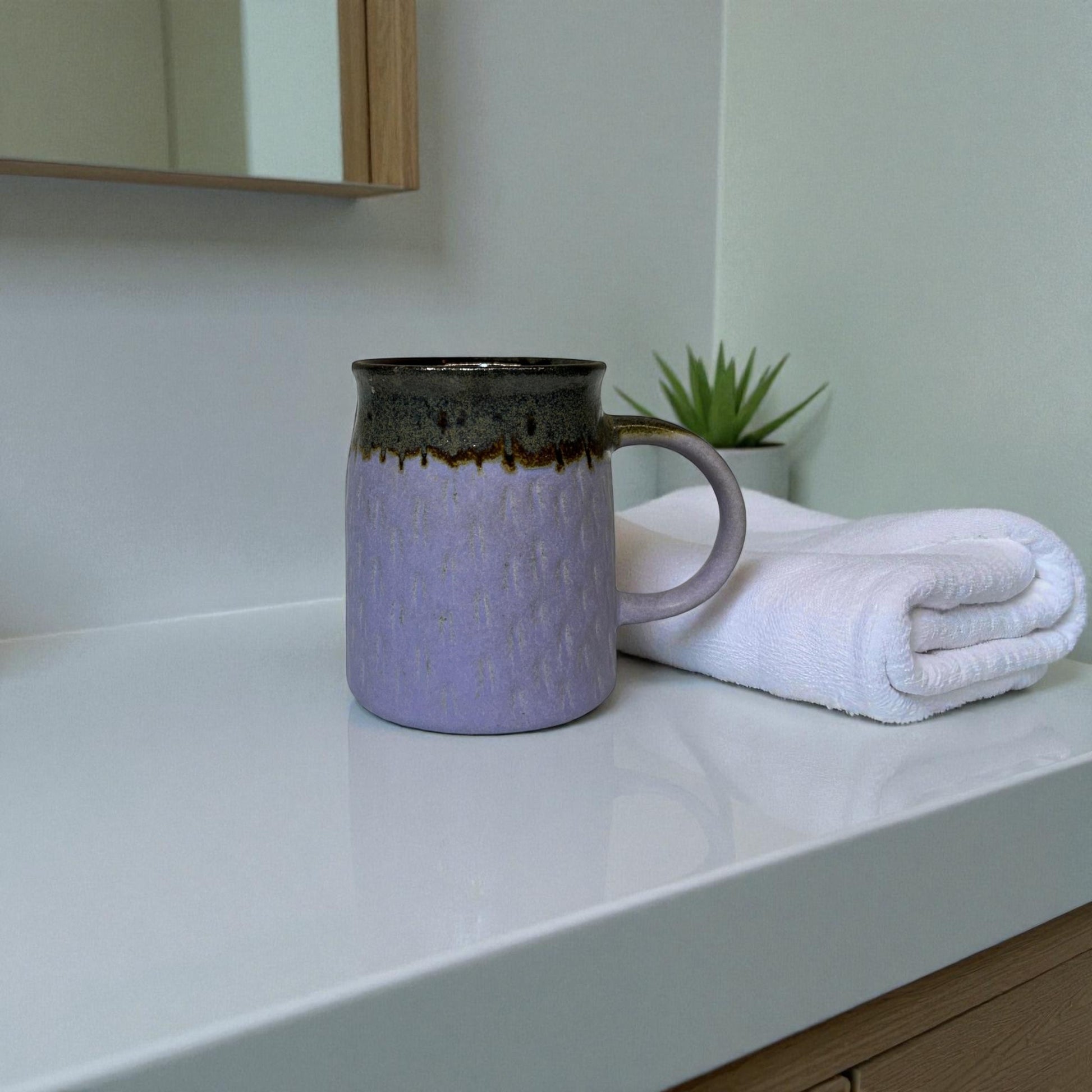 Purple mug with brown accents on a white countertop next to a folded white towel.