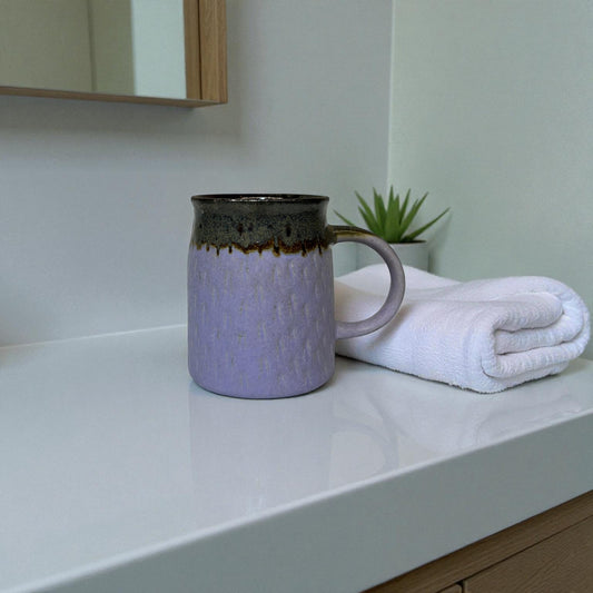 Purple mug with brown accents on a white countertop next to a folded white towel.
