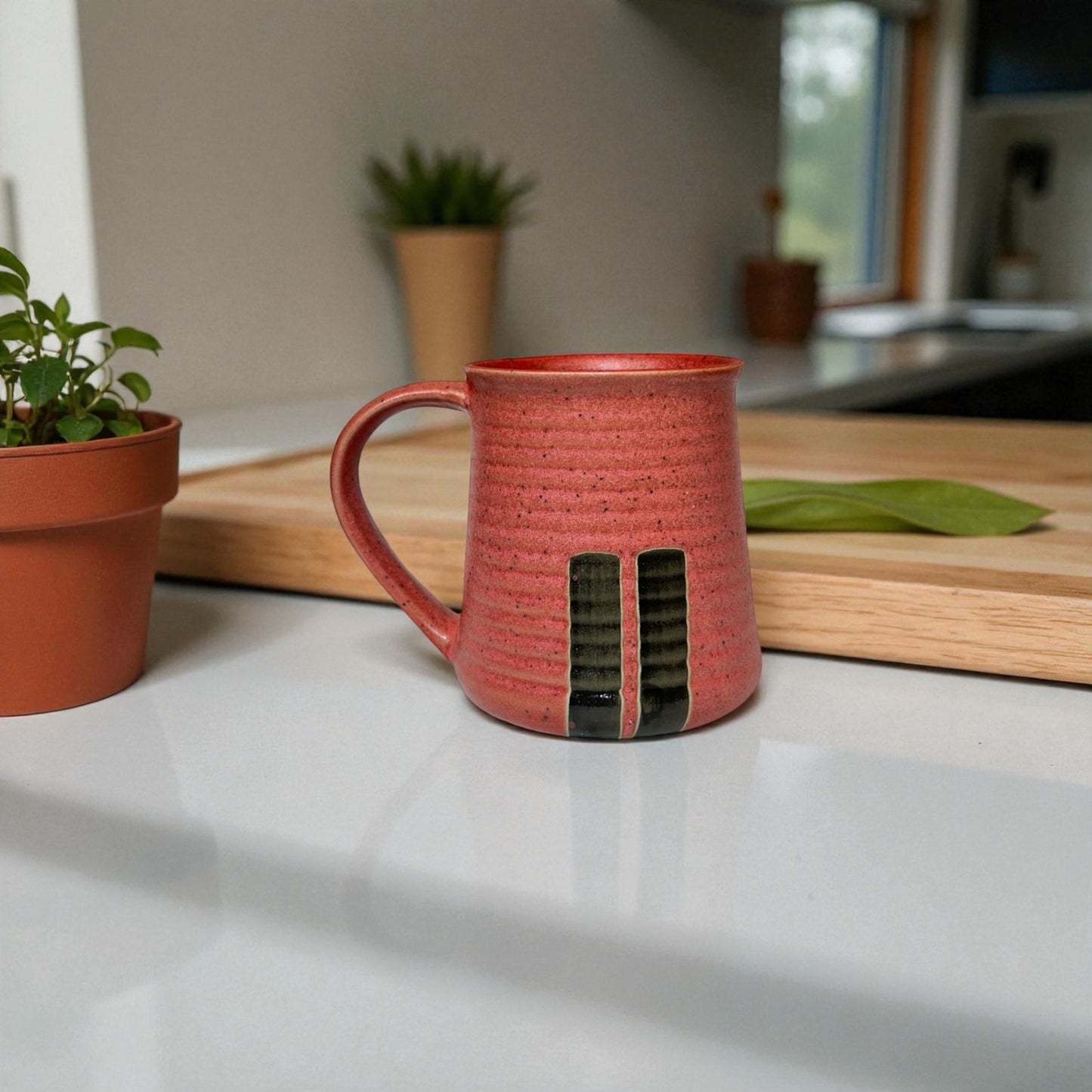 Red ceramic mug on a kitchen counter with plants and a cutting board in the background