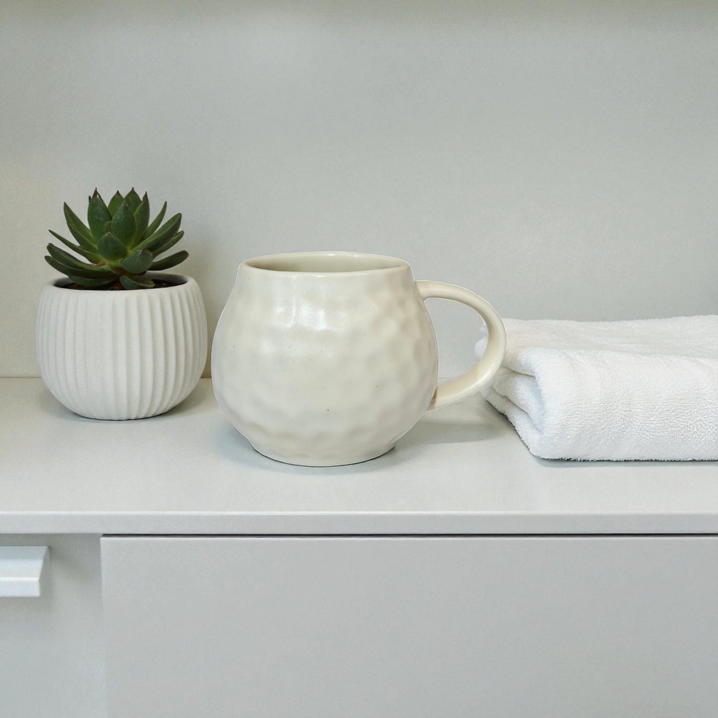 White ceramic mug and small plant on a white surface with a light gray background