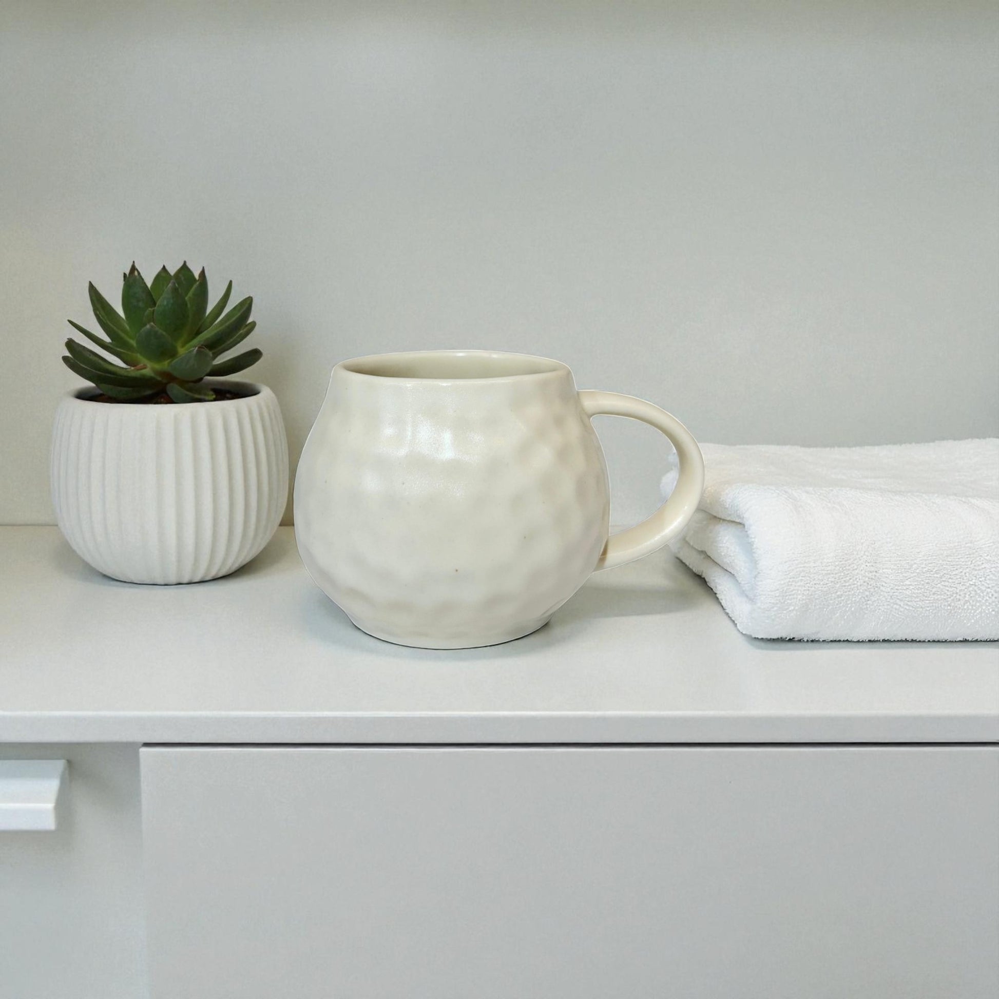 White ceramic mug and small plant on a white surface with a light gray background