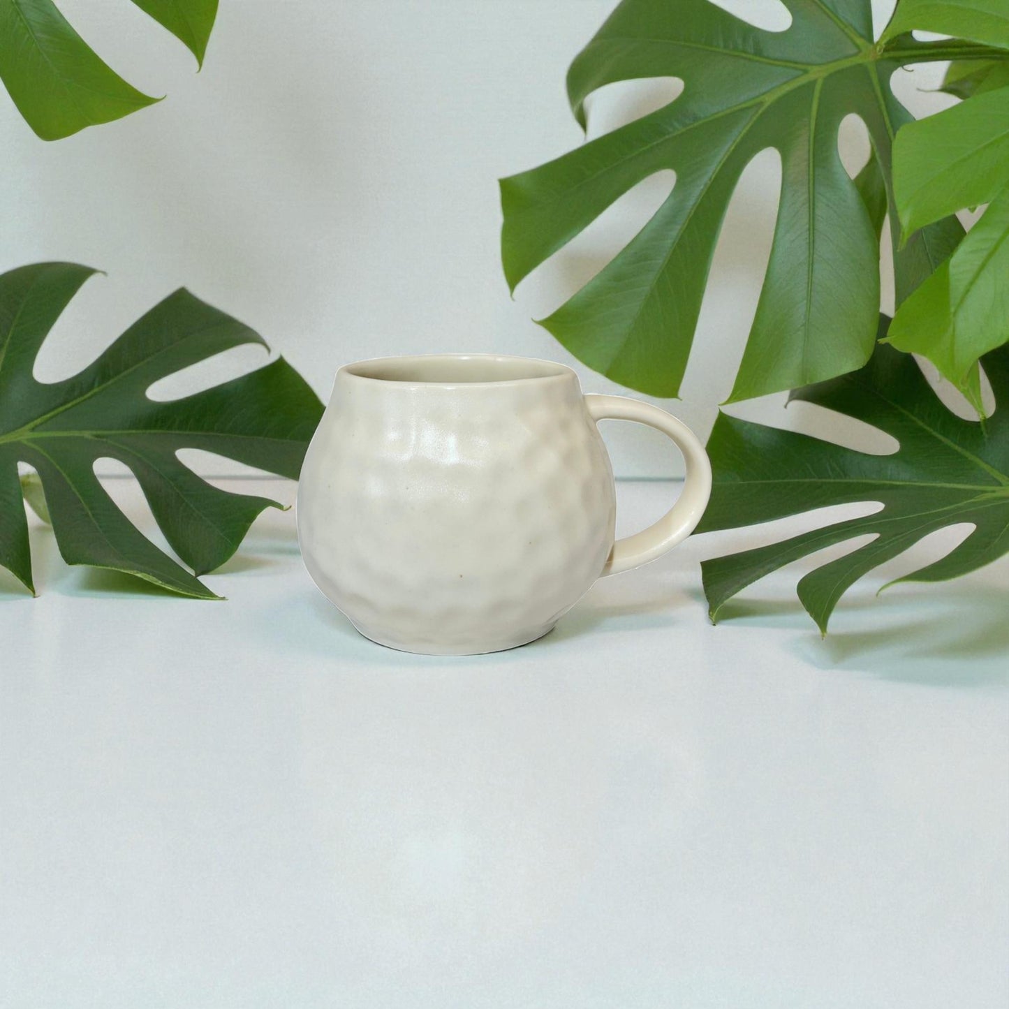 White ceramic mug on a light surface with green leaves in the background