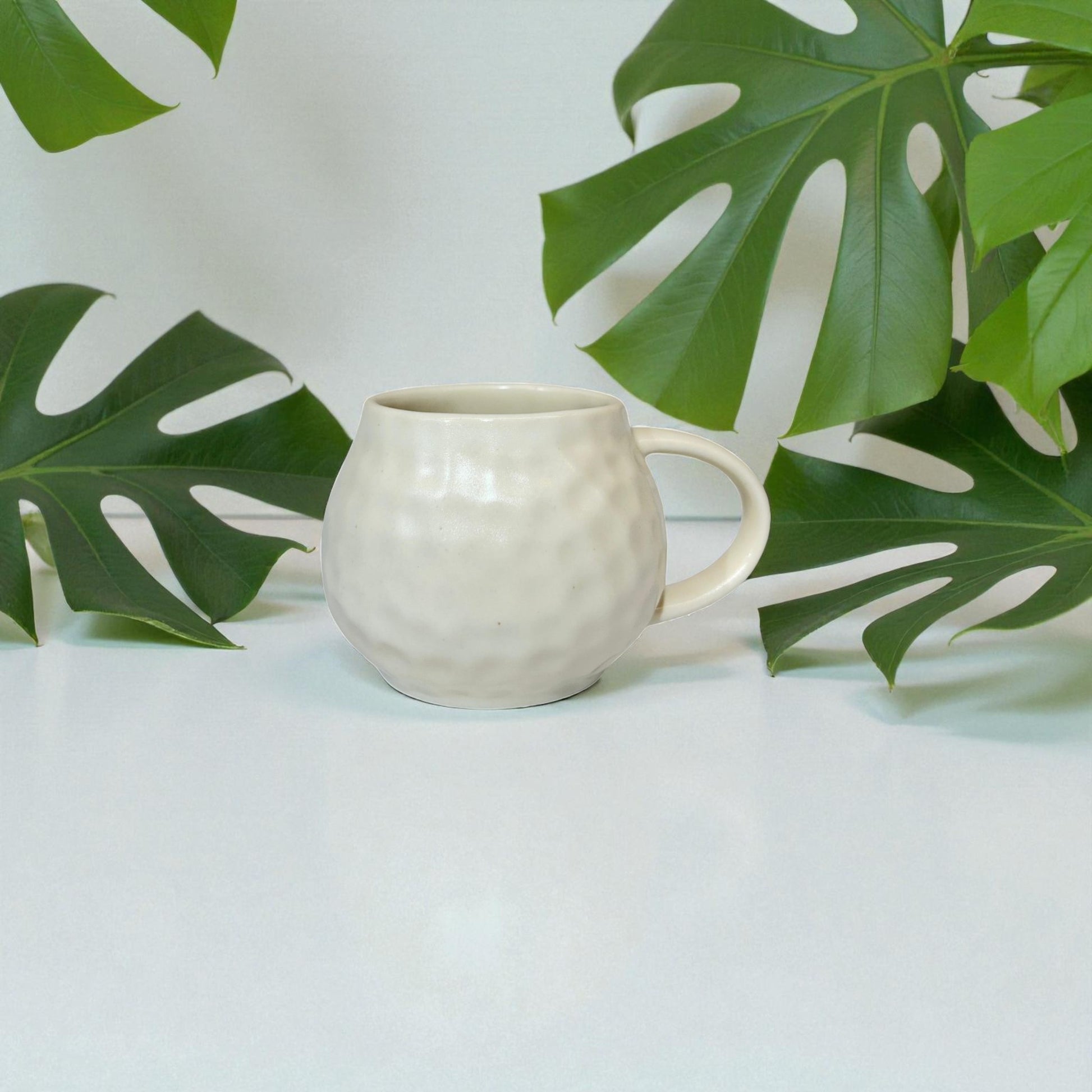 White ceramic mug on a light surface with green leaves in the background