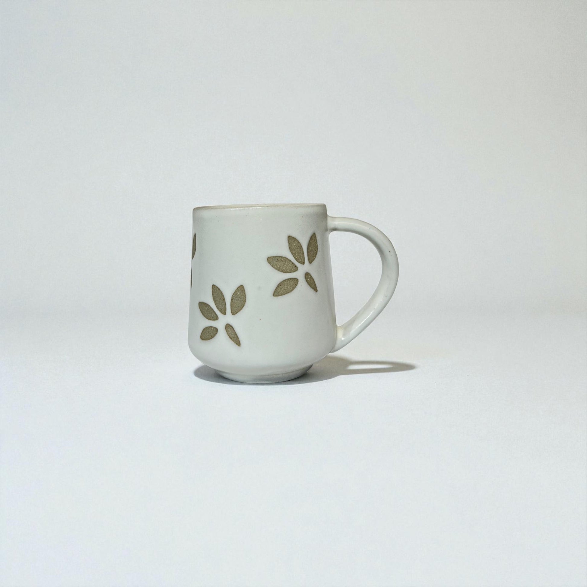 White ceramic mug with green leaf patterns on a light gray background