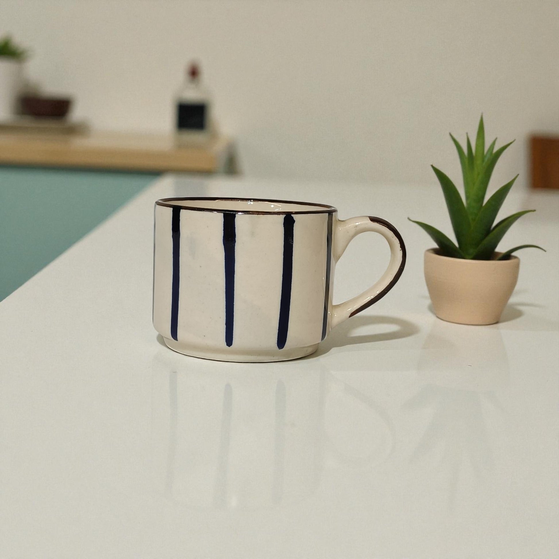 White mug with black stripes on a white surface next to a plant