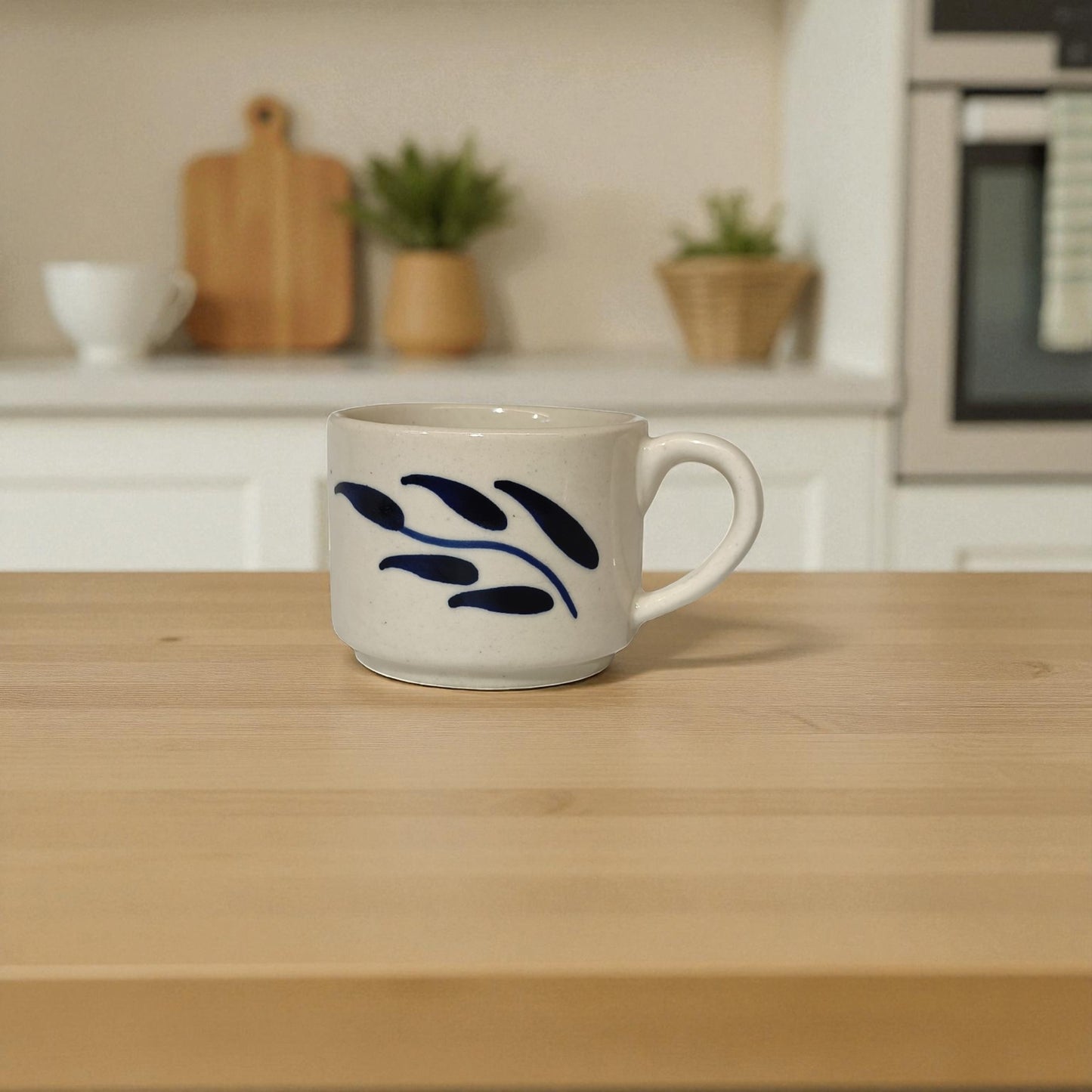 White mug with blue leaf design on a wooden table in a kitchen setting