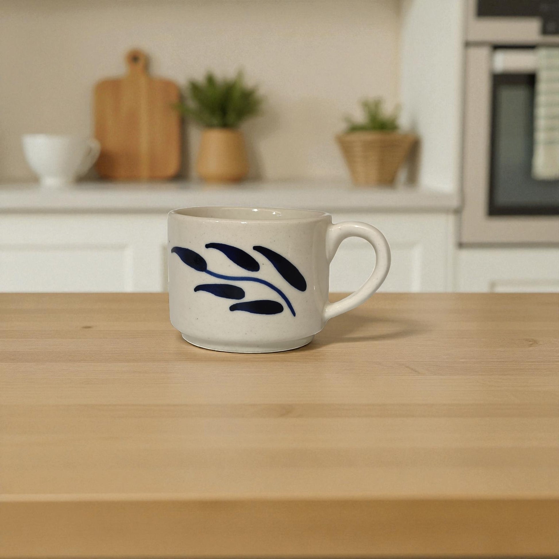 White mug with blue leaf design on a wooden table in a kitchen setting