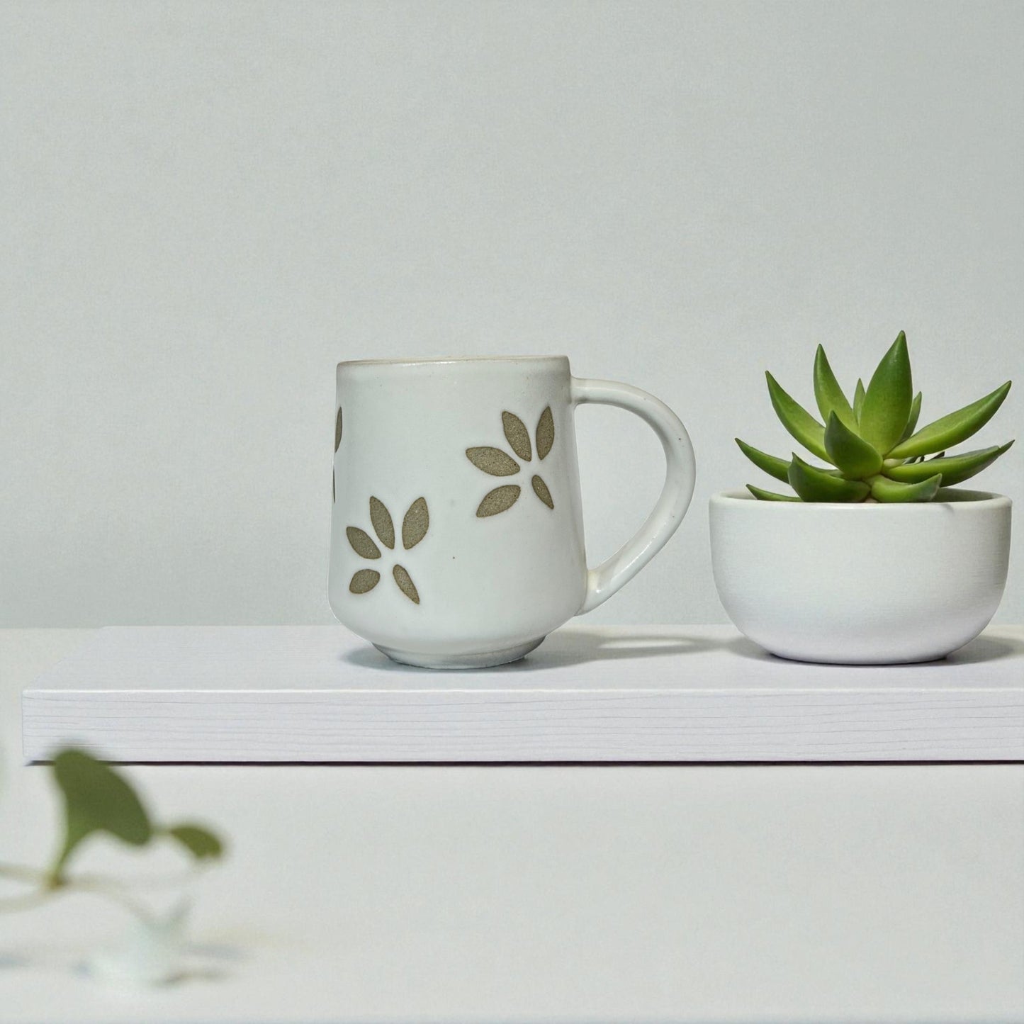 White mug with floral design and small potted plant on a white surface