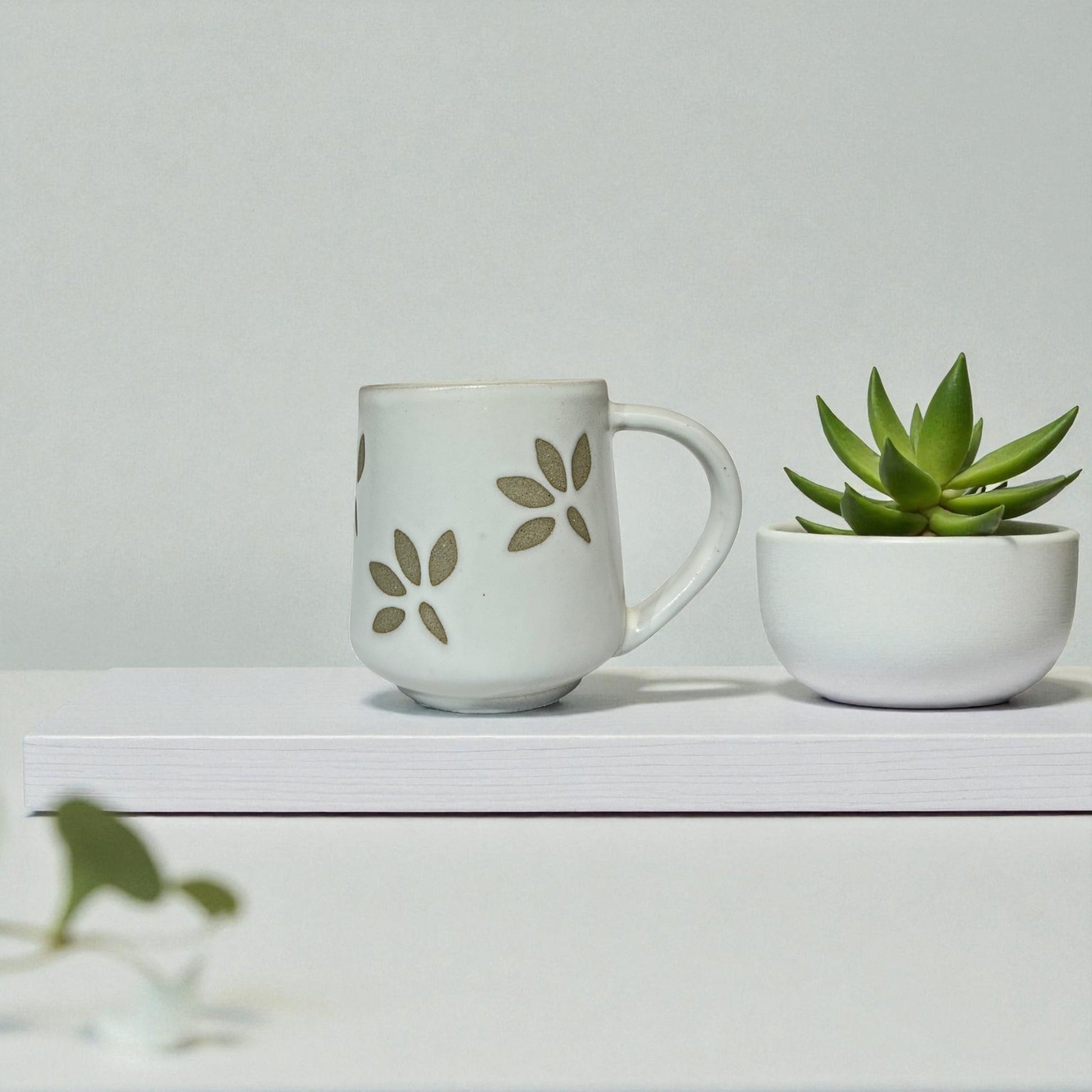 White mug with floral design and small potted plant on a white surface